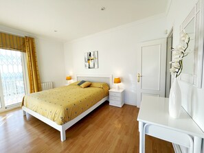 Une chambre à coucher comprenant un lit, des tables de chevet, un bureau, une chaise, une fenêtre avec des rideaux et une porte.