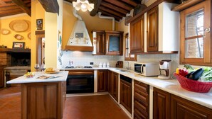 Une cuisine avec des meubles de rangement en bois, un four encastré, un four à micro-ondes et un panier rouge rempli de légumes posé sur le plan de travail.