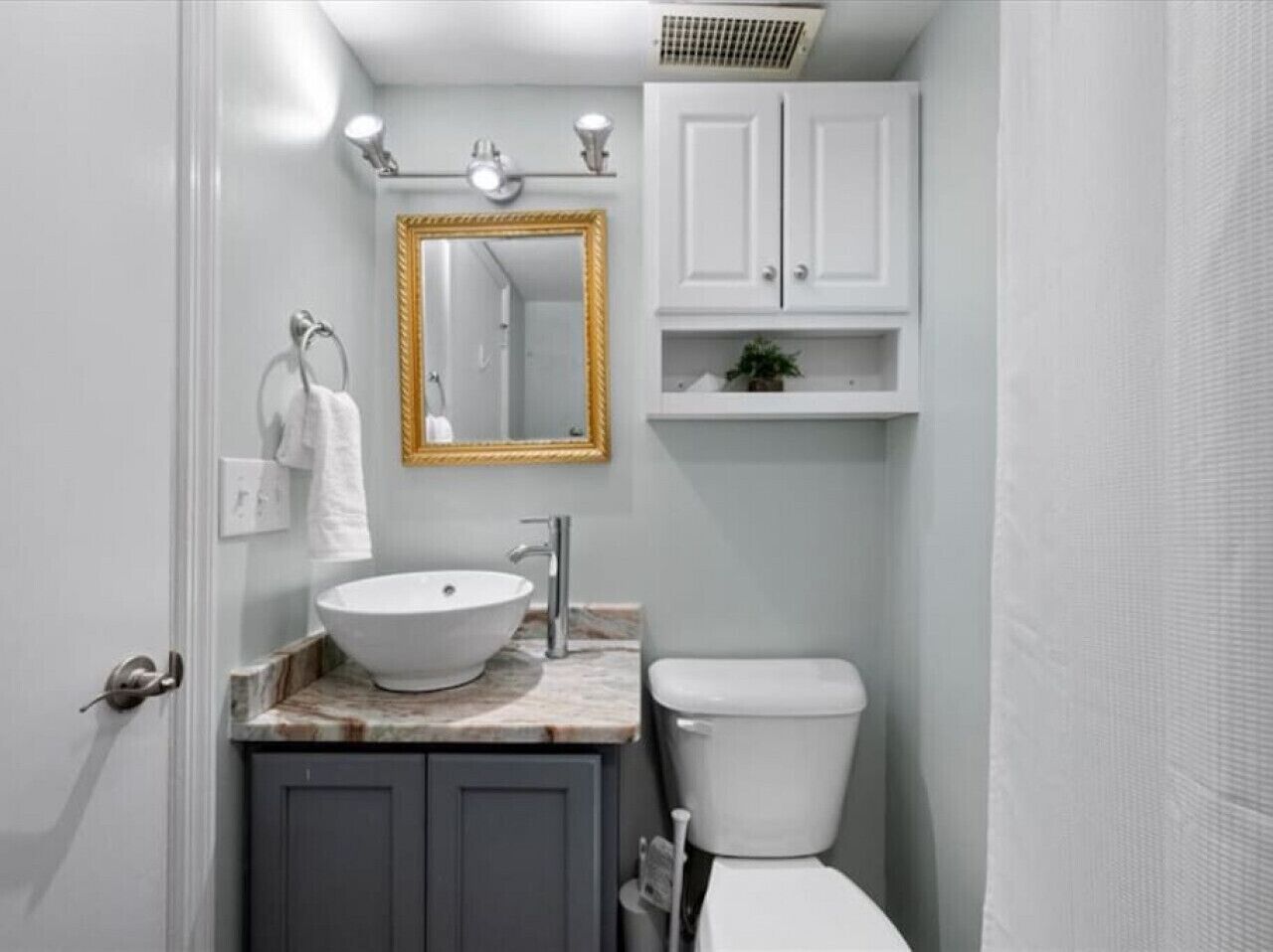 A bathroom with a white sink, a gold-framed mirror, a white toilet, and a cabinet above the sink.