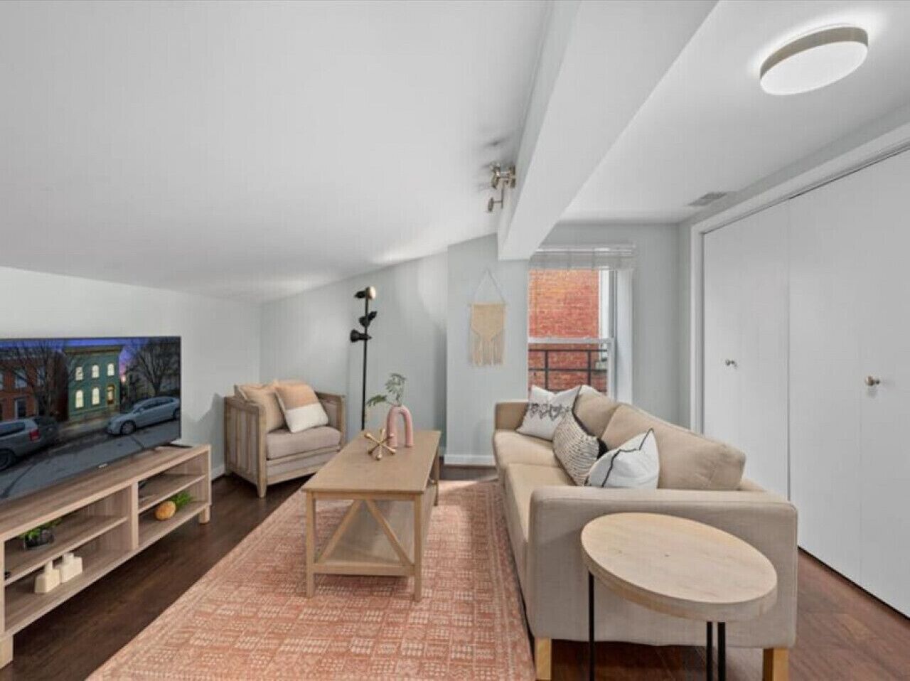 A modern living room with a flat-screen TV, a beige sofa, a wooden coffee table, and a round side table.