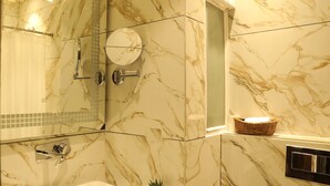 Une salle de bain avec des murs en marbre, une douche en verre, un lavabo et un panier en osier posé sur le comptoir.
