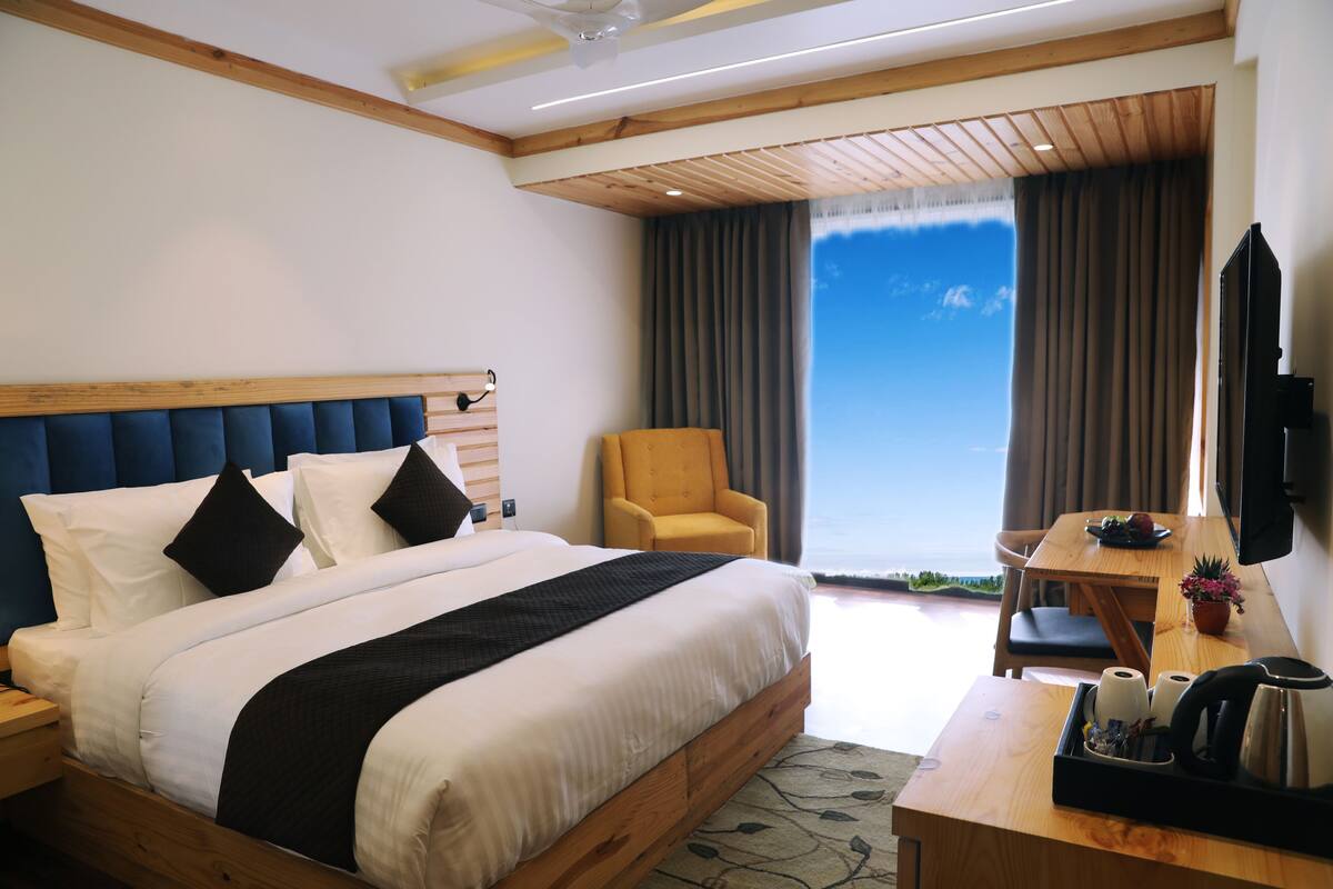 Un hotel moderno con una cama grande, un cabecero de madera, un escritorio con una silla, un televisor y vistas al mar.