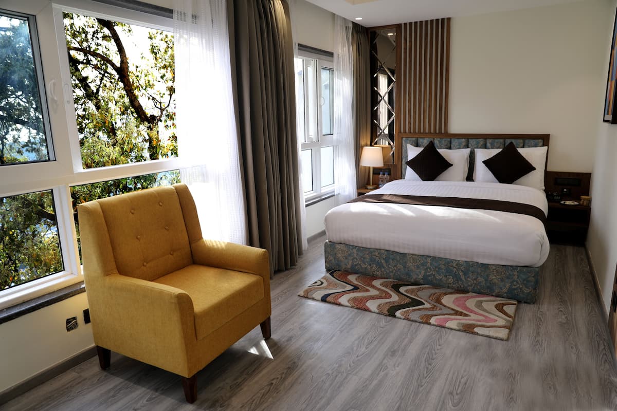 Habitación de hotel con una cama grande, un sofá, una ventana con cortinas y vistas a árboles.
