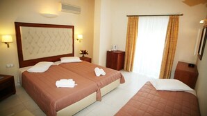Quarto de hotel com duas camas, uma cabeceira grande, luminárias de cabeceira, mesa de cabeceira, uma mesinha de madeira e uma janela com cortinas.