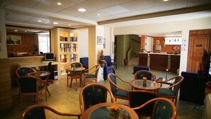 Um saguão de hotel com várias áreas de estar, um balcão de recepção e uma estante de livros.