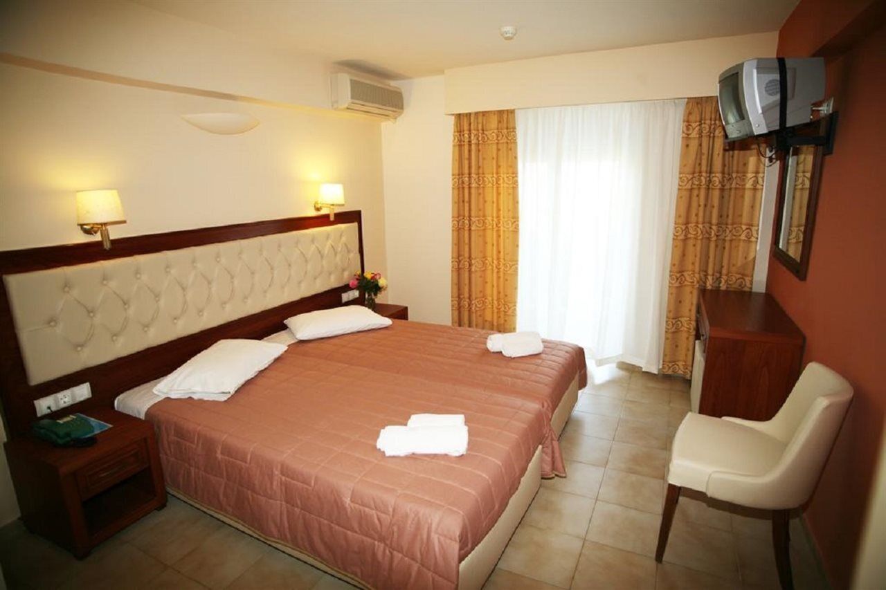 A hotel room with a large bed, two bedside tables, a chair, a TV mounted on the wall, and a window with curtains.