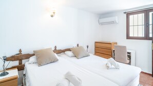 Ein Hotelzimmer mit zwei Betten, einem Holzschrank, einem Nachttisch, einer Lampe, einer Klimaanlage und einem Fenster mit Jalousien.