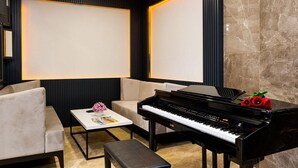 A modern living room with a black piano, a beige sofa, a small coffee table with a magazine, and a decorative flower vase. - Four Sides Hotel (Istanbul)