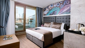 A hotel room with a large bed, a glass door leading to a balcony, a marble wall, and a painting above the bed. - Four Sides Hotel (Istanbul)