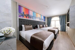 Une chambre d’hôtel avec deux lits, une fresque représentant un paysage urbain, un vase de fleurs et une vue sur la ville.