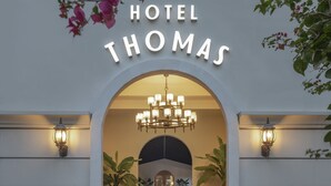 La entrada del Hotel Thomas, con un camino de ladrillo que conduce a la entrada principal, flanqueada por macetas y un gran arco.