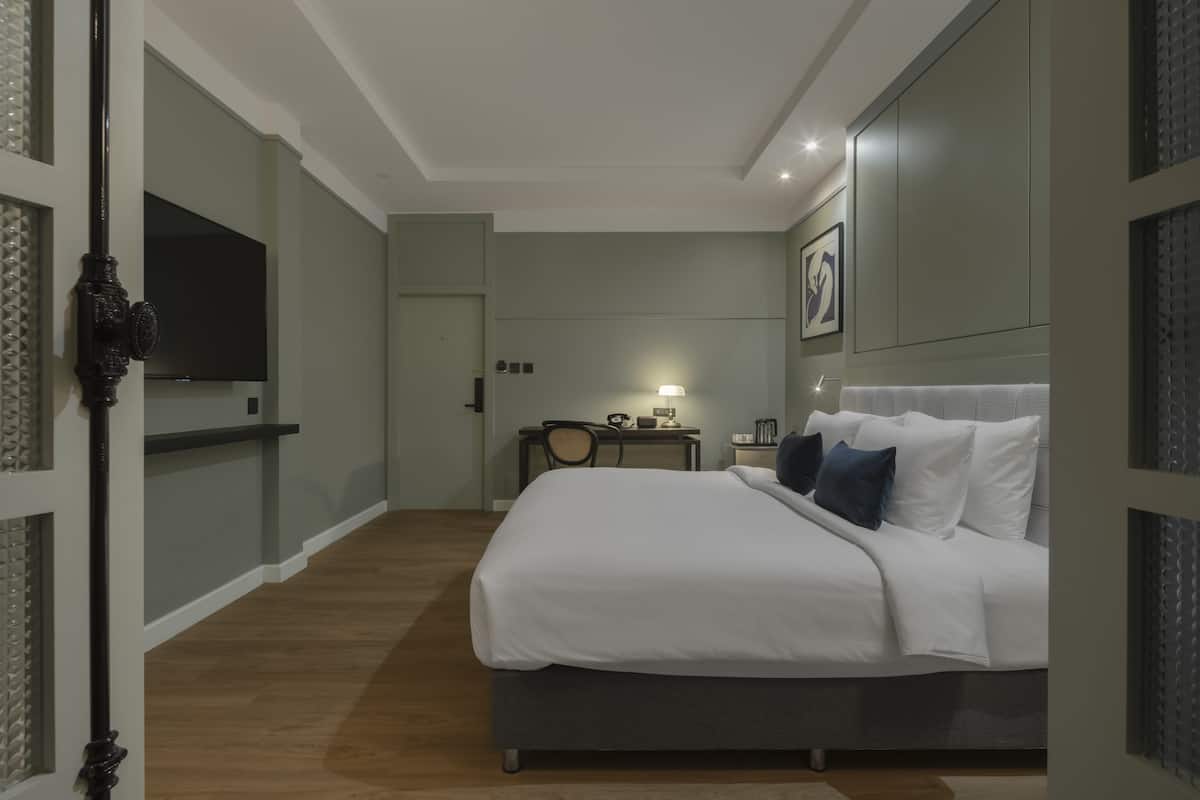 A modern hotel room with a large bed, a desk with a chair, a flat-screen TV, and a wall-mounted artwork.