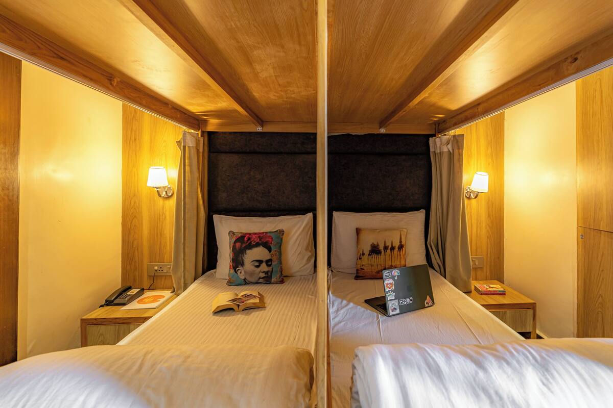 Ein Hotelzimmer mit zwei Betten, hölzernen Kopfteilen, Nachttischlampen, einem Telefon, einem Laptop und einem Buch auf einem der Betten.