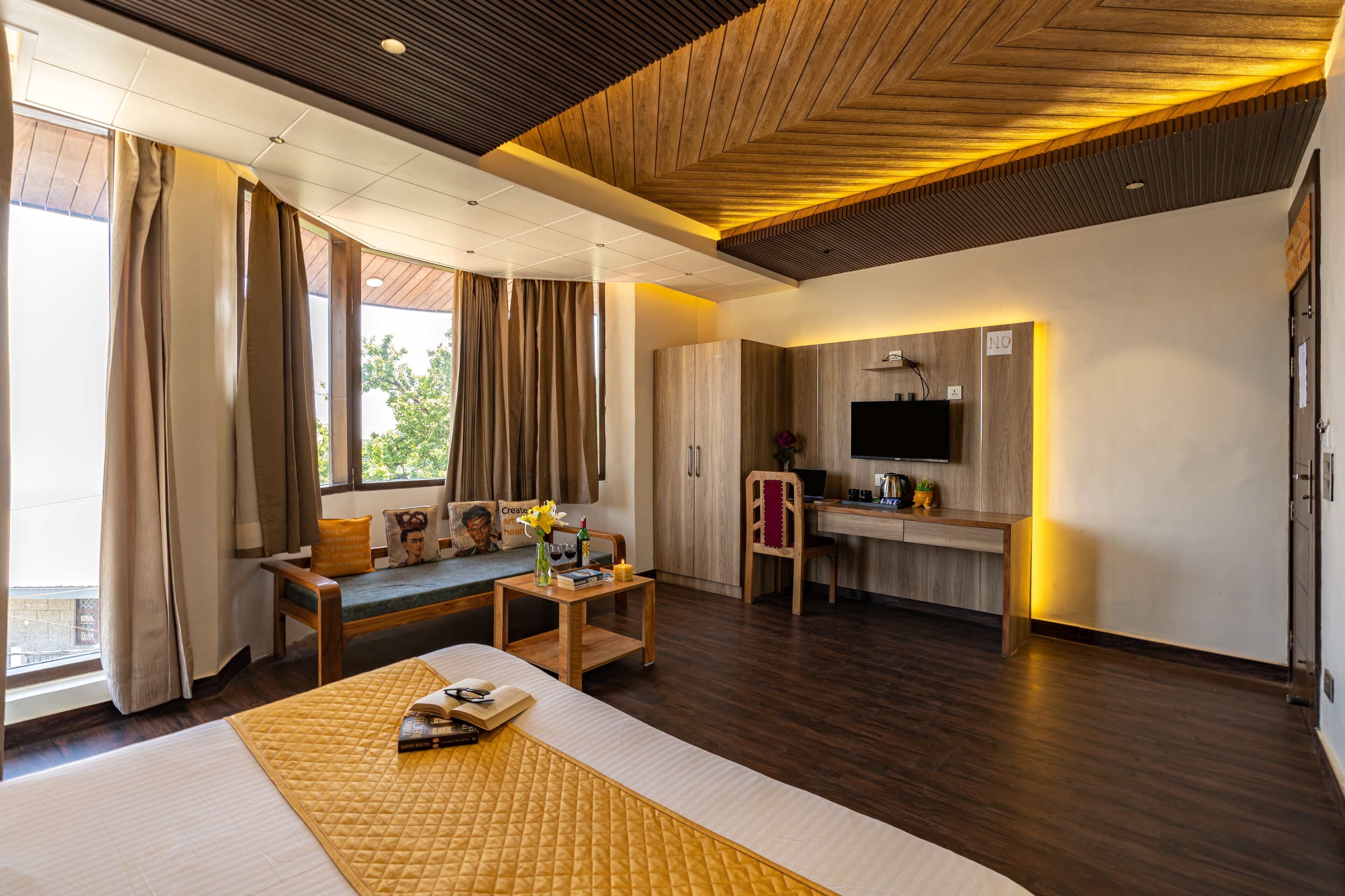 A modern hotel room with a large bed, a seating area with a table, a television, and a kitchenette.