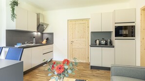 Une cuisine moderne avec des meubles blancs, une porte en bois et un four à micro-ondes. On y trouve une petite table sur laquelle est posé un vase de fleurs et une télécommande.