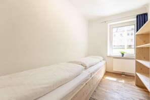 Pequeña habitación individual con cama, ventana, suelo de madera y radiador.