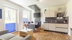 Un salon moderne comprenant un canapé, une table basse et un coin repas avec des chaises et une table. Il y a aussi une cuisine équipée d’une cuisinière, d’un évier et de placards.