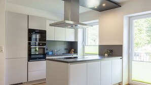 A modern kitchen with a central island, built-in oven, and a large window providing natural light. - Apartment in Alps with Stunning Views (No Deposit) (Eisenerz)
