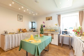 A dining area with a green table, white tablecloth, and various food items. There are two refrigerators, a microwave, and a coffee machine. The room has wooden floors and white walls. - Beautiful cottage in Styria near lake (No Deposit) (Eisenerz)