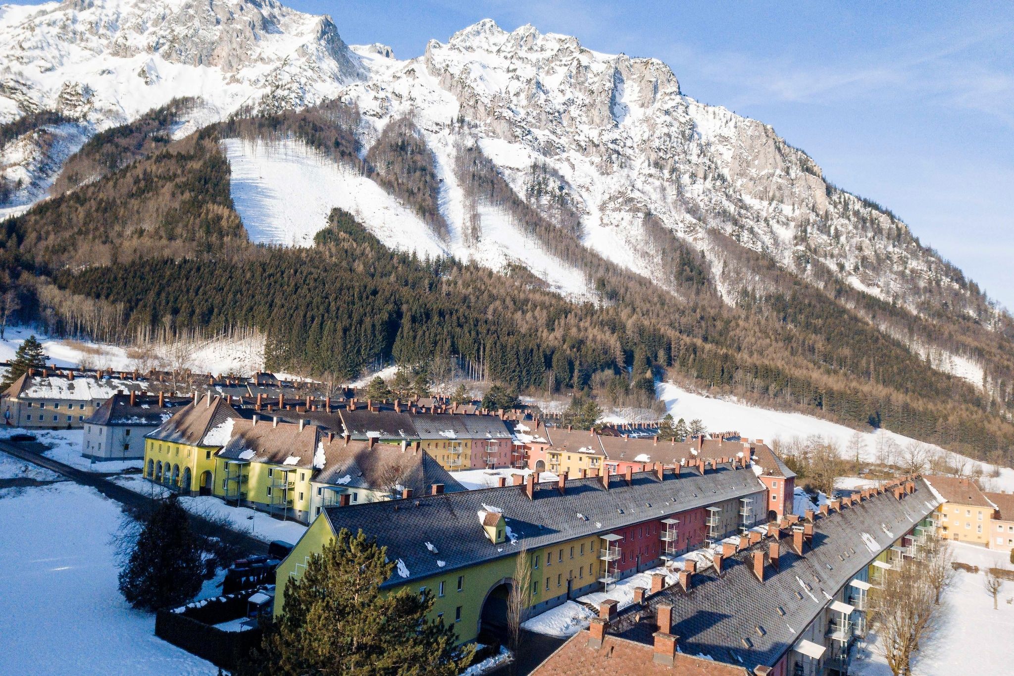 A town with colorful buildings, a river, and snow-covered mountains in the background.