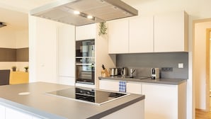 A modern kitchen with white cabinetry, a built-in oven, a stovetop, and a small island with a sink. - Beautiful cottage in Styria near lake (No Deposit) (Eisenerz)