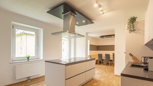 A modern kitchen with a central island, a built-in stove, and a window with a plant. - Beautiful cottage in Styria near lake (No Deposit) (Eisenerz)