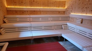 Una sauna con varios bancos, paredes de madera y un tapete rojo en el suelo.