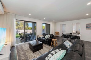 Een moderne woonkamer met een bank, een voetenbankje en een eethoek met stoelen.