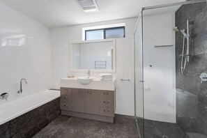 Un baño moderno con bañera, lavamanos con espejo, cabina de ducha y ventana.