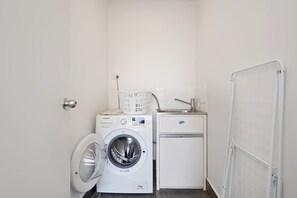 Ein kleiner Waschraum mit einer Waschmaschine, einem kleinen Kühlschrank und einem Wäscheständer aus Metall.