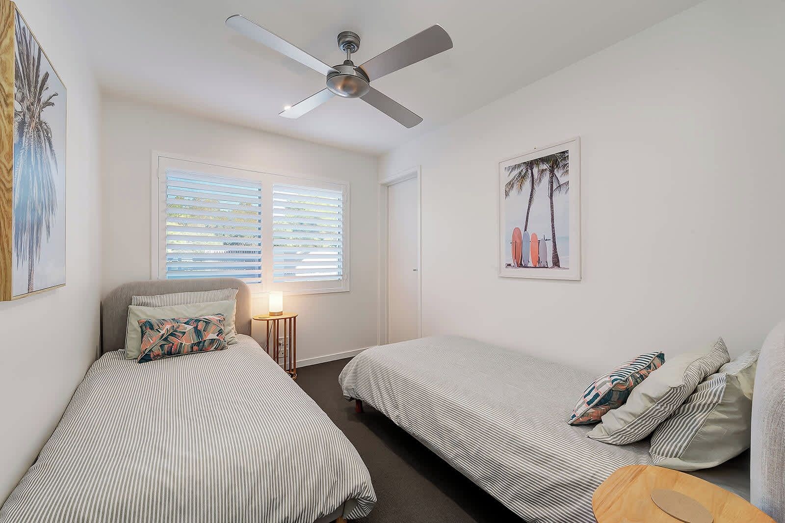 A bedroom with two single beds, a ceiling fan, a nightstand, and a framed picture on the wall.