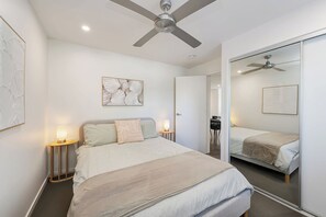 Un dormitorio moderno con cama, lámparas de noche, ventilador de techo y un espejo grande.
