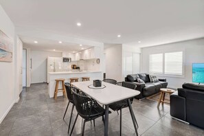 Een modern appartement met een eetgedeelte, keuken, woonkamer en een televisie waarop een strandscène te zien is.