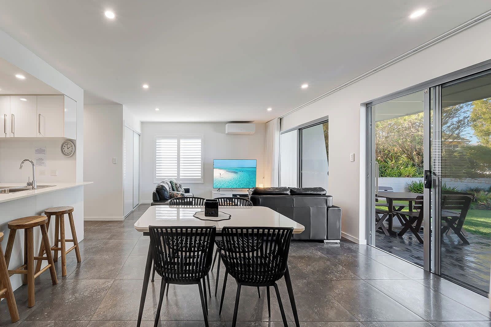 A modern kitchen with a dining area, a large TV, and a sliding glass door to a patio.