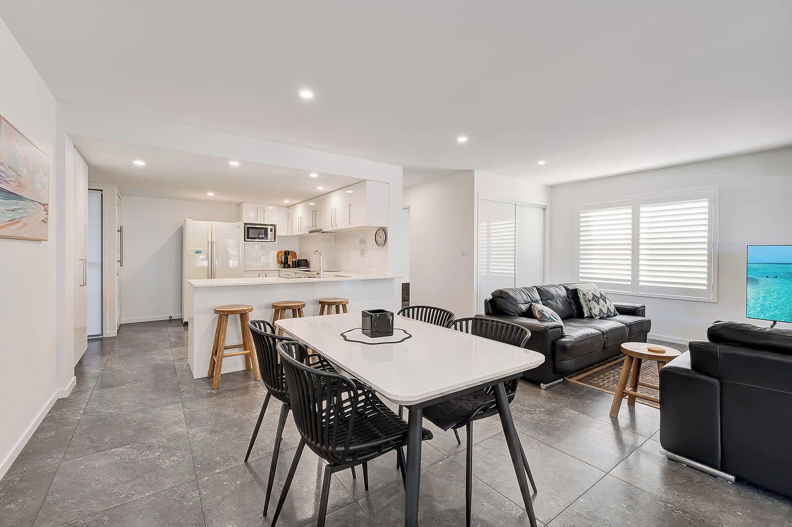 A modern apartment with a dining area, kitchen, living room, and a TV displaying a beach scene.