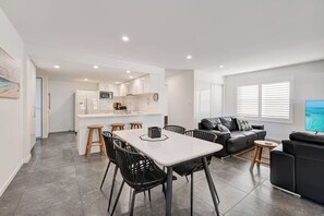 Eine moderne Wohnung mit Essbereich, Küche, Wohnzimmer und einem Fernseher, der eine Strandansicht zeigt.