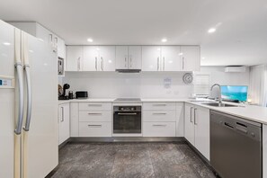 Een moderne keuken met witte kasten, een inbouwoven, een vaatwasser en een groot raam met uitzicht.
