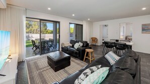 A modern living room with a sofa, ottoman, and dining area with chairs. - Coochin Court | Walk to Dicky Beach (DICKY BEACH)