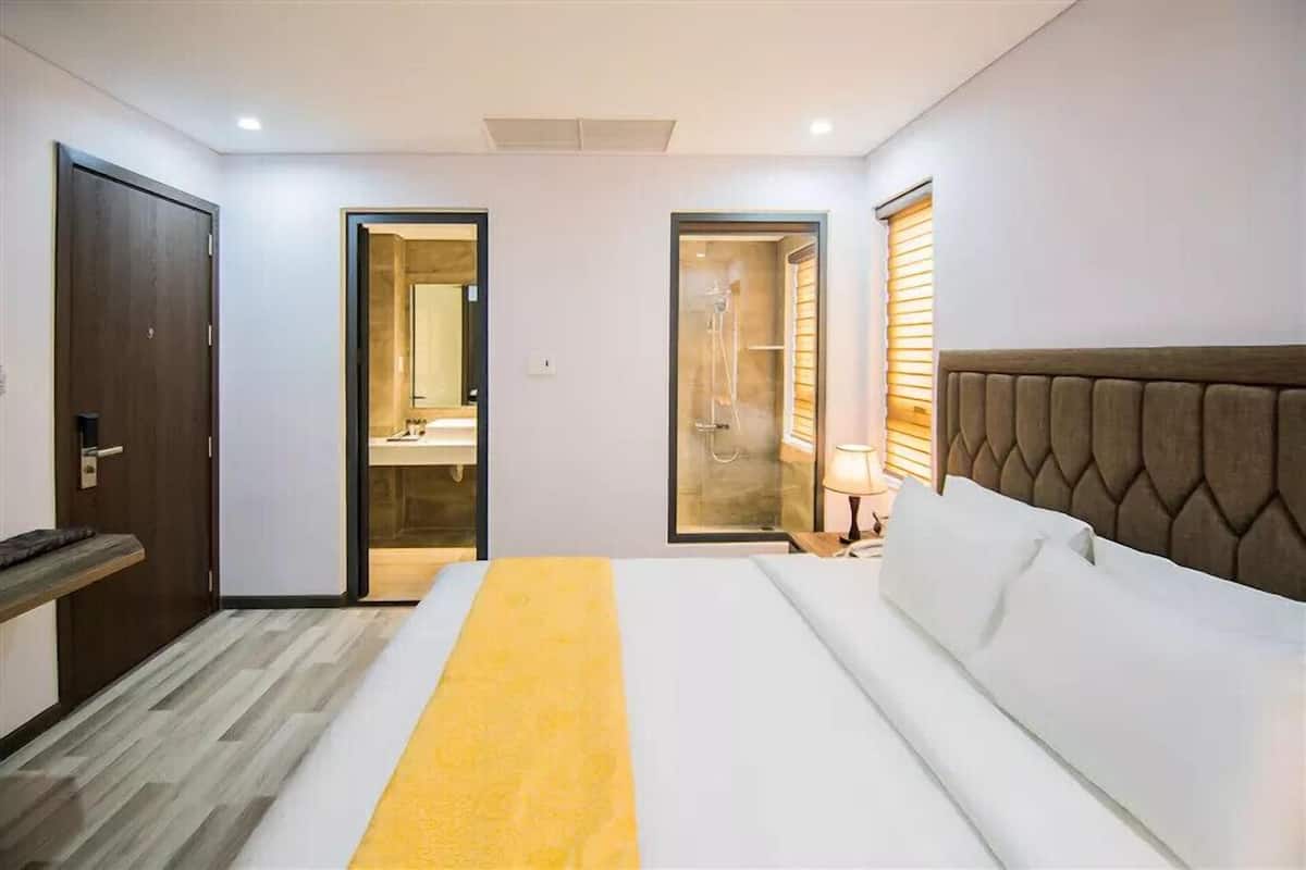 A hotel room with a bed, a bedside table, a mirror, a shower area, and a door.