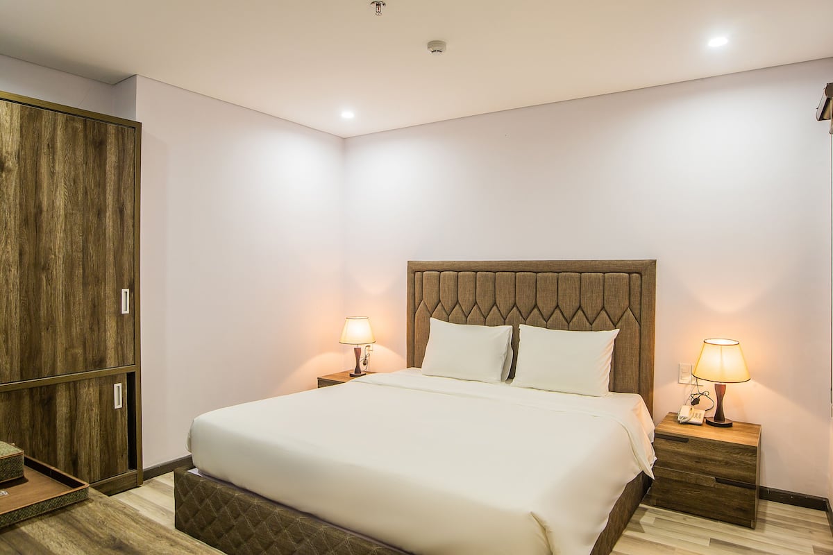 A neatly made bed with a wooden headboard, two bedside tables with lamps, and a wooden wardrobe.