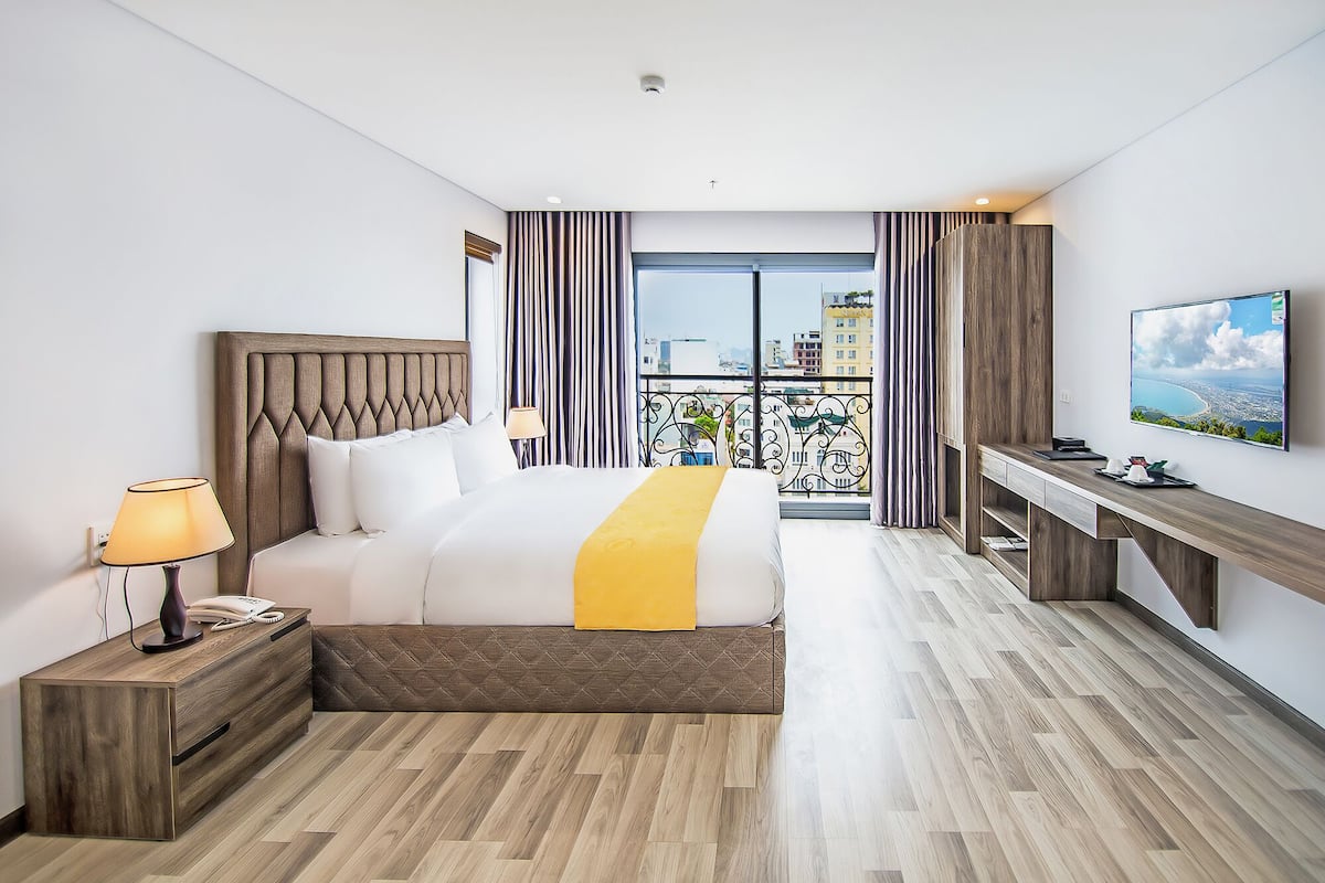 A hotel room with a bed, bedside table, lamp, desk, and a TV.