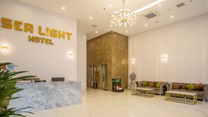 A hotel reception area with a marble reception desk, a chandelier, and a seating area with sofas and a fan. - SEA LIGHT HOTEL DA NANG (Da Nang)