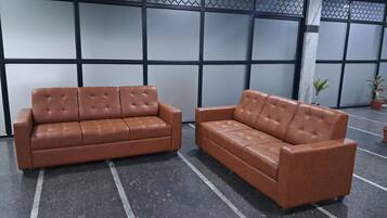 Two brown leather sofas with a grid-patterned wall and potted plants in the background.