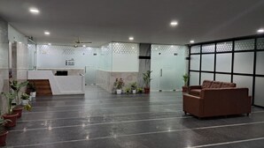 A reception area with a reception desk, a brown sofa, and potted plants. - The Balcony Hotel (Hyderabad)