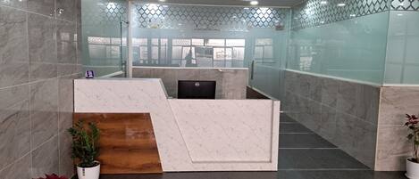 Un área de recepción con un mostrador de mármol, una pared decorativa de madera y una computadora Dell.