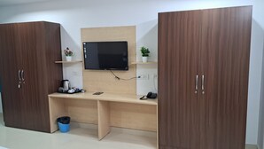 A room with a wooden desk, a flat-screen TV, two potted plants, a trash bin, and a telephone. - The Balcony Hotel (Hyderabad)
