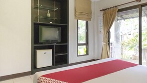 A hotel room with a bed, a television on a shelf, a small refrigerator, and a window with curtains. - OYO 1046 OYO 1046 Noppharat Resort (Krabi)