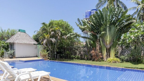 A swimming pool with tiled blue edges, surrounded by white lounge chairs and tropical vegetation. - OYO 1046 OYO 1046 Noppharat Resort (Krabi)