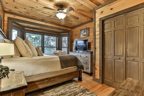 A bedroom with a bed, a ceiling fan, a TV, and a large wooden door.