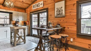 A wooden interior with a kitchen area, a dining table with stools, and a sign indicating 'MTNS.' - Cherry Log Sky Bear | Cherry Log, GA (Blue Ridge)